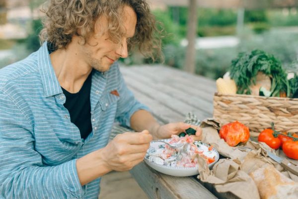 A man enjoying a healthy meal with fresh vegetables at an outdoor picnic table.