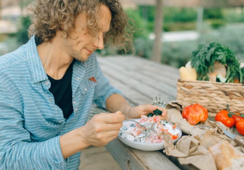 A man enjoying a healthy meal with fresh vegetables at an outdoor picnic table.
